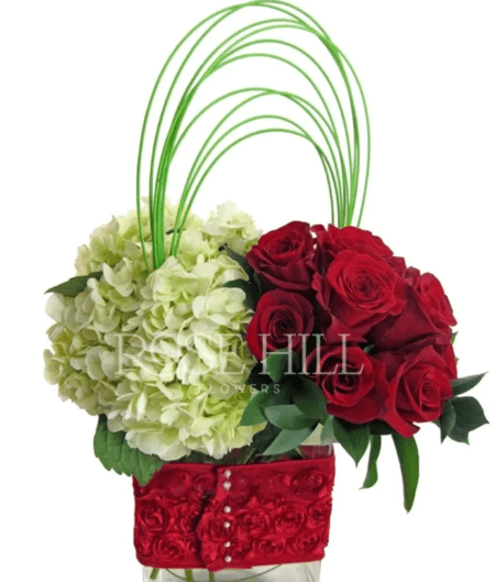 Artfully arranged dozen roses and hydrangea in a cube with fabulous red wrap.