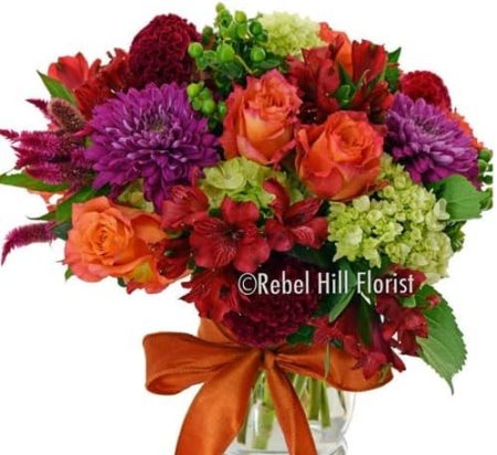 Fronds of feathery millet and puffy, rooster-red coxcomb bring a touch of harvest color to a lovely mix of orange roses, and more, arranged in a graceful clear glass vase.